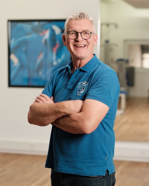 Mitarbeiter mit grauem kurzen Haar, Brille und blauem Poloshirt