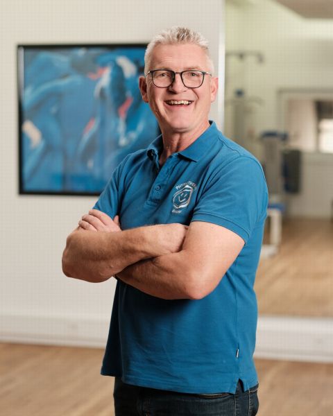 Mitarbeiter mit grauem kurzen Haar, Brille und blauem Poloshirt