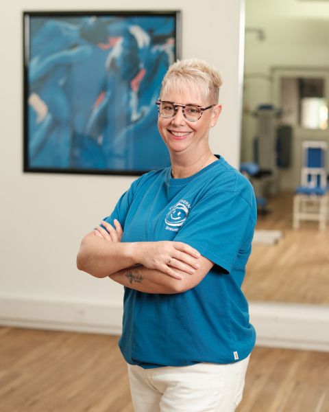 Mitarbeiterin mit kurzem blondem Haar und blauem Praxis-T-Shirt