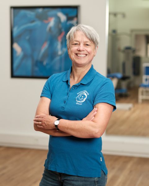 Mitarbeiterin mit grauem kurzem Haar in blauem Praxis-Poloshirt