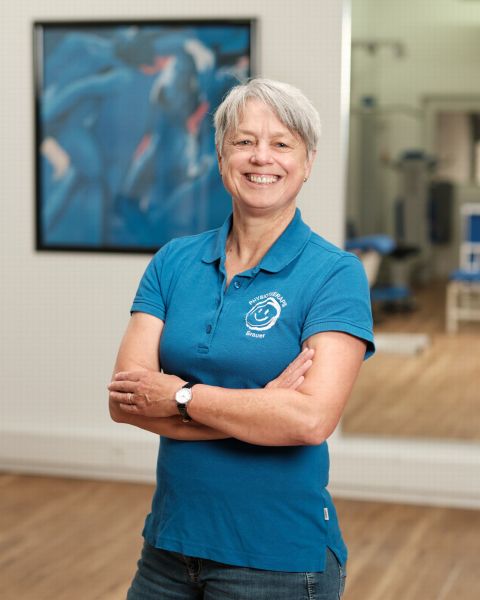 Mitarbeiterin mit grauem kurzem Haar in blauem Praxis-Poloshirt
