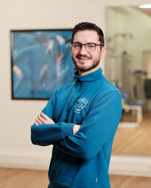 Mitarbeiter mit dunklem kurzen Haar, Brille und blauem Zip-Pullover